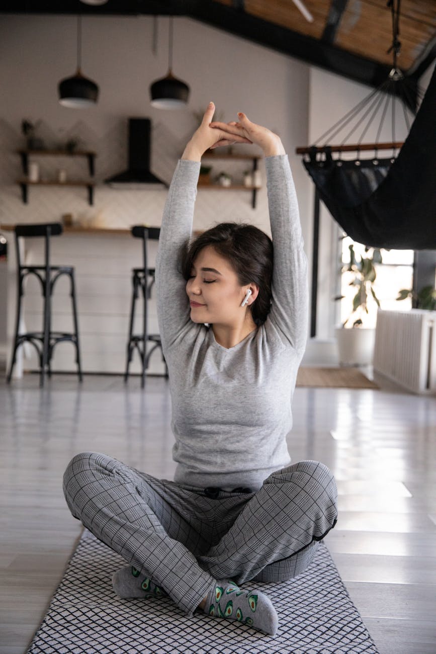 ethnic woman in earbuds sitting in lotus pose at home